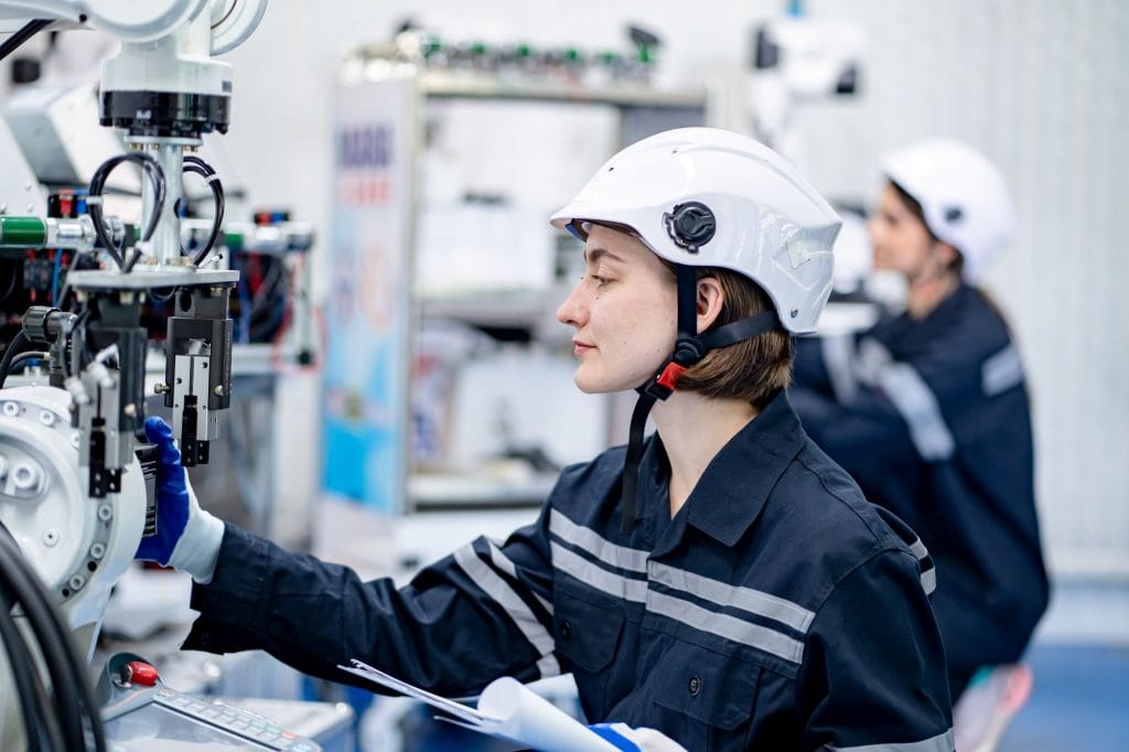 Pracownica w kasku ochronnym i ubraniu roboczym obsługująca nowoczesną maszynę produkcyjną.